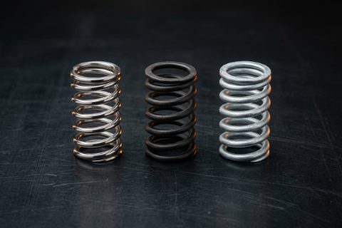Três molas especiais em inox, liga escura e galvanizado lado a lado.