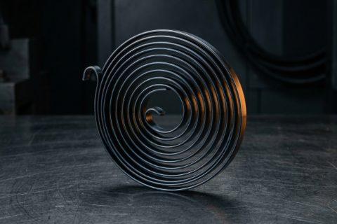 Mola espiral plana de fita de aço sobre bancada de aço escura.